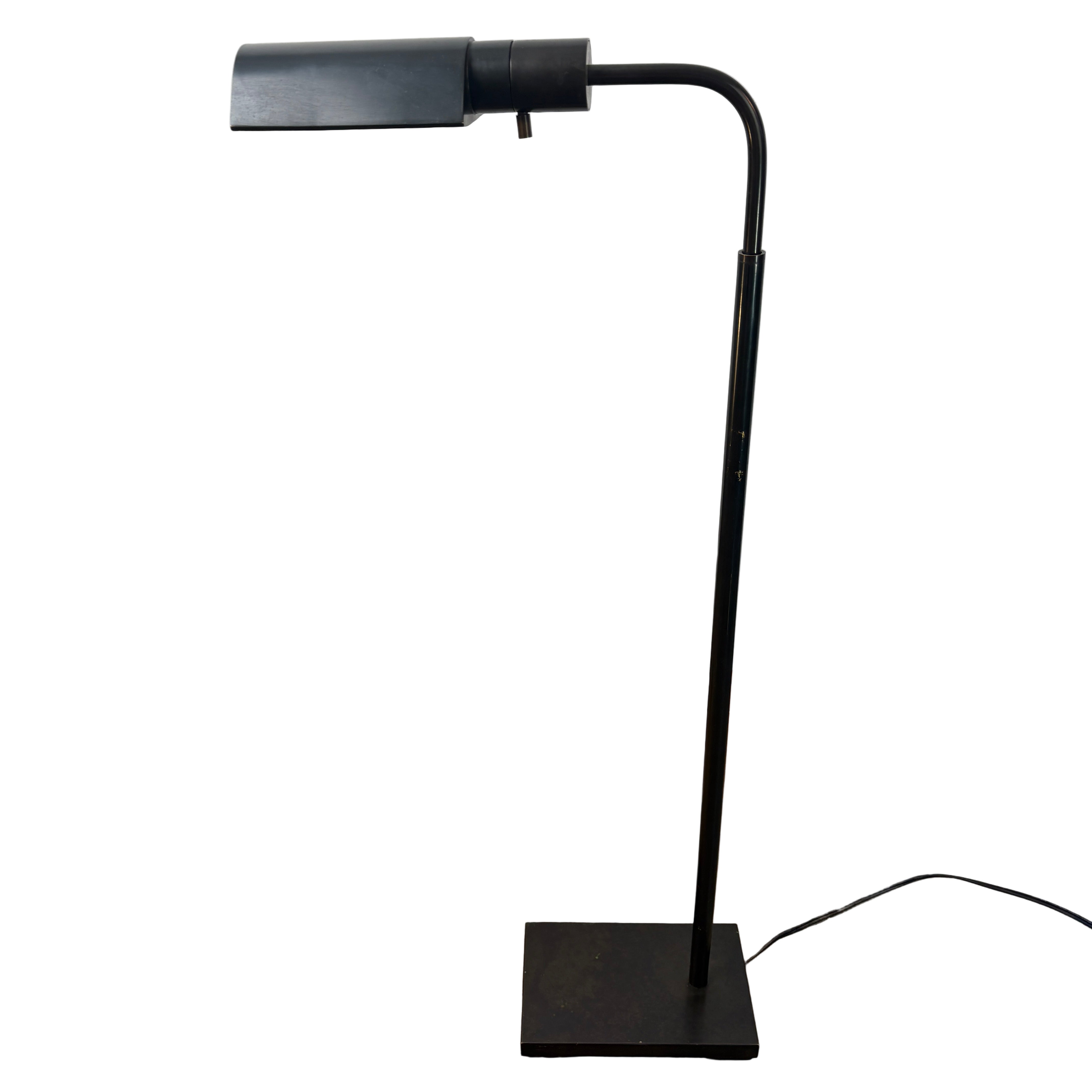 Black adjustable desk lamp on a concrete floor with a white wall background