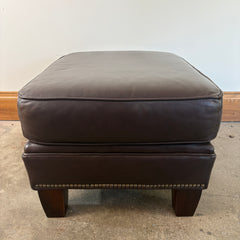 Brown leather ottoman on a concrete floor with a plain wall background