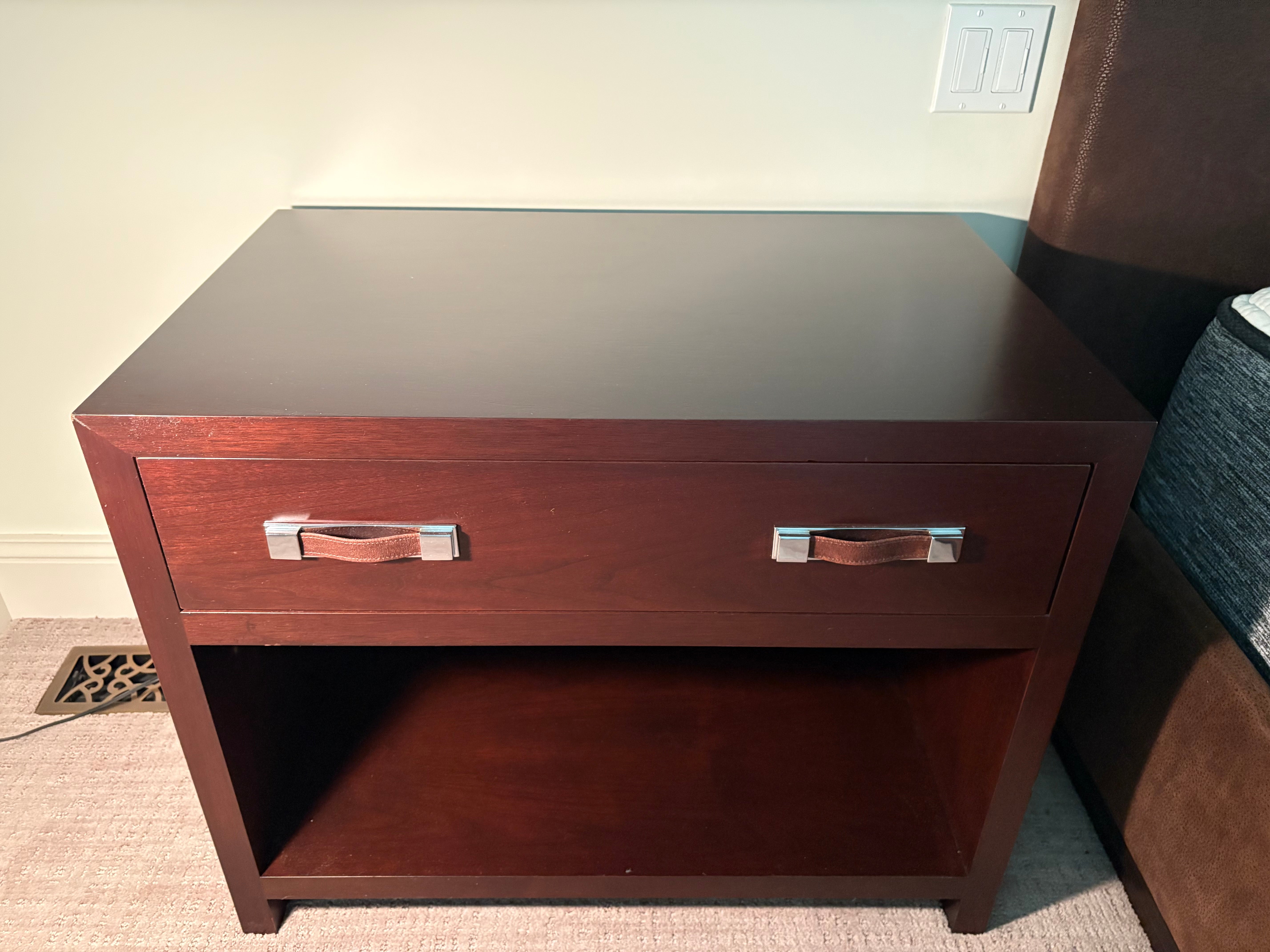 Wooden nightstand with a single drawer and open shelf against a neutral wall.