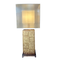 Tall decorative lamp with a textured square design on a wooden table in a showroom setting.